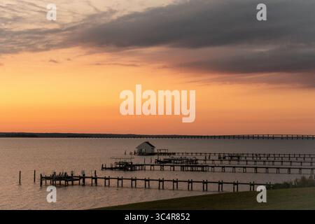 Scène paisible en bord de mer au lever du soleil, avec des jetées, un hangar à bateaux, et un beau ciel dégradée sur l'eau calme Banque D'Images