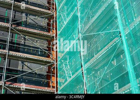 Un bâtiment en rénovation montre des échafaudages exposés, des panneaux isolants et des filets verts de protection pour la sécurité des travailleurs Banque D'Images