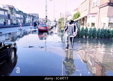 Floding Zandvoortselaan, Zandvoortselaan, 22-11-1999 Whizgle News, Dutch Desk, pays-Bas, 1950-2000 Une personne portant un équipement de protection navigue dans une rue inondée, où l'eau reflète les bâtiments et les véhicules environnants. Les cônes de circulation et le matériel de construction sont visibles à l'arrière-plan, ce qui indique les efforts continus pour gérer la situation. Banque D'Images