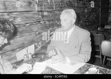 Mr. de Jong avec tasse de café, Persons, 23-06-1971 Whizgle News, Dutch Desk, pays-Bas, 1950-2000 Un homme en costume engage une conversation à une table, faisant des gestes avec ses mains assis en face d'une autre personne qui prend des notes. Le cadre comprend des murs en bois et une table ornée d'une nappe à motifs, ainsi que des tasses à café et des salières et poivrons visibles à proximité. Banque D'Images