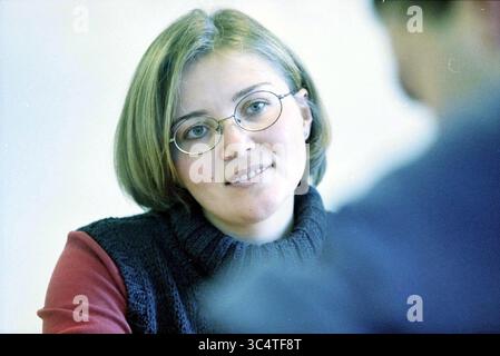 Anne - Lotte Bartels Haarlem, Haarlem, pays-Bas, 14-11-2001 Whizgle News, Dutch Desk, pays-Bas, 1950-2000 Une femme aux cheveux courts et clairs et aux lunettes écoute attentivement pendant une conversation, affichant une expression réfléchie. Elle porte un haut sans manches sombre sur une chemise rouge à manches longues, suggérant un comportement décontracté mais composé. Banque D'Images
