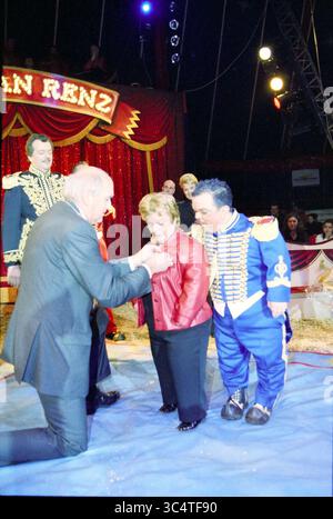 Décoration royale A. Olivier Circus Renz, 21-12-2002 Whizgle News, Dutch Desk, pays-Bas, 1950-2000 Un groupe d'artistes en costumes élaborés se réunit sous une tente de cirque. Une figure s'agenouille pour présenter une fleur à une femme dans une veste rouge, tandis que d'autres interprètes regardent, souriants et engagés dans l'instant présent. L'atmosphère vibrante est remplie d'excitation et de camaraderie. Banque D'Images