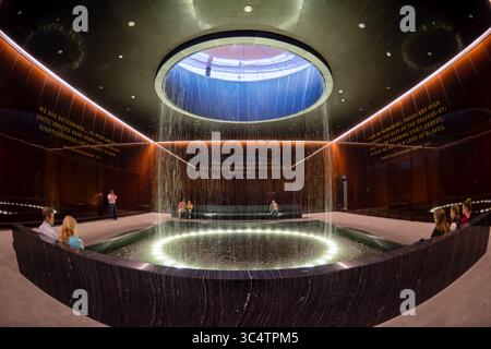 Musée national d'histoire et de culture afro-américaines Cour contemplative Washington DC | WASHINGTON D.C., États-Unis — Une fontaine cylindrique tombe à travers un oculus éclairé dans la cour contemplative du Musée national d'histoire et de culture afro-américaines. La salle circulaire au niveau 0 du Concourse est entourée de verre de cuivre-bronze caramel par Bendheim et gravée de citations de Nelson Mandela et Martin Luther King Jr., conçu comme une pause méditative entre les galeries d'histoire en dessous de niveau et les galeries de culture ci-dessus. Banque D'Images