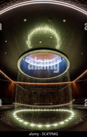 Musée national d'histoire et de culture afro-américaines Cour contemplative Washington DC | WASHINGTON D.C., États-Unis — Une vue grand angle capture l'anneau complet de l'oculus de la Cour contemplative et de la piscine à l'intérieur du Musée national d'histoire et de culture afro-américaines. L'eau tombe en continu du plafond éclairé s'ouvrant dans le bassin réfléchissant ci-dessous, un élément de design entouré par le verre de cuivre-bronze caramel de Bendheim et gravé de citations de l'époque des droits civiques choisies par les architectes du musée. Banque D'Images