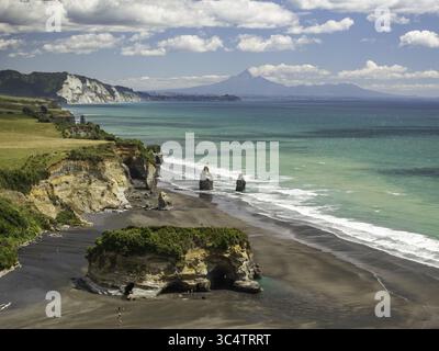 Vue aérienne du paysage côtier spectaculaire où le sable noir rencontre les eaux turquoises, encadrée par la silhouette lointaine du mont Taranaki, New Plymout Banque D'Images