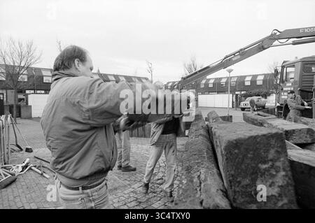 Rénovation de Helmplein, IJmuiden, IJmuiden, pays-Bas, 14-01-1994 Whizgle News, Dutch Desk, pays-Bas, 1950-2000 Un groupe de travailleurs s'engage dans une tâche manuelle impliquant de grandes poutres en bois, une personne soulevant une poutre tandis que d'autres sont positionnées à proximité, aidant ou préparant éventuellement les prochaines étapes du projet. Un véhicule et une machinerie sont visibles en arrière-plan, indiquant un effort de construction ou de rénovation. Banque D'Images