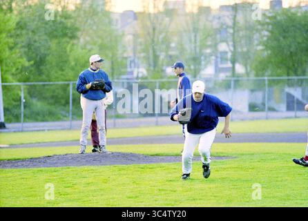 La première formation de l'équipe néerlandaise de baseball, 13-05-1997 Whizgle News, Dutch Desk, pays-Bas, 1950-2000 Un groupe de joueurs de baseball est engagé dans la pratique sur un terrain herbeux. Un joueur court vers la caméra, tandis que d'autres sont positionnés sur le monticule et sur le terrain extérieur, se préparant pour le prochain jeu. La toile de fond présente des arbres et des bâtiments, indiquant un cadre urbain. Banque D'Images