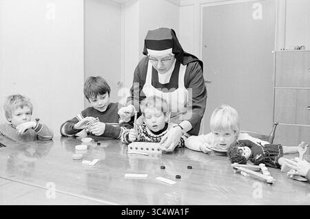 Intérieur de la maison d'enfants de Schapenduinen., intérieur, 23-12-1969 Whizgle News, Dutch Desk, pays-Bas, 1950-2000 Un groupe de quatre enfants se réunit autour d'une table, concentrés intensément comme une religieuse les aide dans un projet créatif impliquant l'artisanat de matériaux. L’atmosphère est une atmosphère de curiosité et de travail d’équipe, car les enfants s’engagent dans des activités pratiques, apprennent et explorent ensemble. Banque D'Images