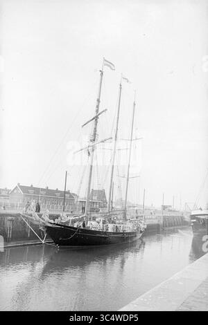 Goélette anglaise, IJmuiden, navires, 16-02-1972 Whizgle News, Dutch Desk, pays-Bas, 1950-2000 Un grand voilier à trois mâts est amarré dans un port calme, ses voiles enroulées et ses drapeaux volants. Les bâtiments environnants bordent le front de mer, créant une scène maritime sereine. Banque D'Images