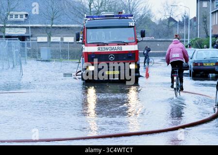 Tuyau d'eau éclaté R. Holkade, 09-03-1998 Whizgle News, Dutch Desk, pays-Bas, 1950-2000 Un camion de pompiers, étiqueté 'BRANDWEER', est stationné dans une zone urbaine inondée tandis qu'un cycliste navigue dans l'eau à proximité. Les bâtiments environnants révèlent un décor de banlieue, avec des véhicules dispersés partiellement submergés. Banque D'Images