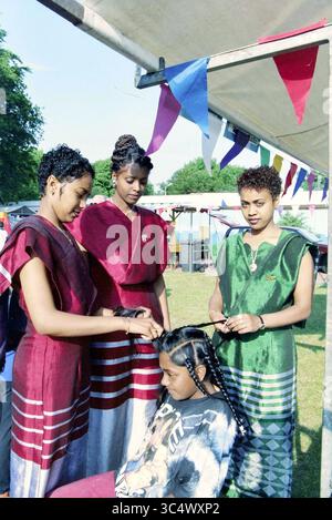 Trois filles éthiopiennes, 17-06-1997 Whizgle News, Dutch Desk, pays-Bas, 1950-2000 Un groupe de trois individus vêtus d'une tenue traditionnelle vibrante tout en coiffant les cheveux d'une personne assise. Le décor présente des drapeaux décoratifs en arrière-plan, créant une atmosphère festive. Banque D'Images