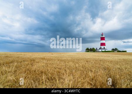 Phare de Happisburgh à Norfolk, Royaume-Uni avec un champ de blé au premier plan à l'approche d'une tempête, tour de phare rouge et blanc, voyage Banque D'Images
