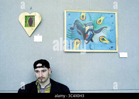 Artists + Work Municipal achats, IJm., IJmuiden, pays-Bas, 19-02-1996 Whizgle News, Dutch Desk, pays-Bas, 1950-2000 Un jeune homme s'assoit soigneusement à côté de deux œuvres d'art : un cadre en bois en forme de coeur contenant une petite pièce, et une peinture colorée présentant une composition abstraite aux formes tourbillonnantes et aux flammes vibrantes. Banque D'Images