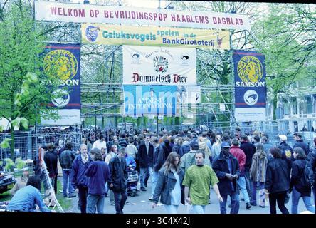 Poupée de libération diverse Haarlem, Haarlem, pays-Bas, 04-05-1998 Whizgle News, Dutch Desk, pays-Bas, 1950-2000 Une scène de festival en plein air animée avec une foule nombreuse, avec des bannières pour diverses organisations et événements. Les arbres offrent une toile de fond naturelle, et les participants sont engagés dans des conversations et des activités, créant une atmosphère de célébration et de camaraderie. Banque D'Images