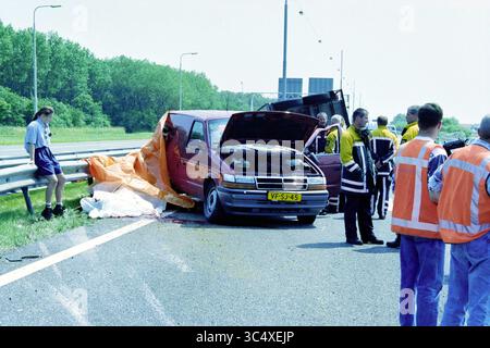 Accident de remorque de cheval, A9, A9, 13-06-1999 Whizgle News, Dutch Desk, pays-Bas, 1950-2000 Une minifourgonnette rouge est garée sur le côté d'une autoroute avec son capot ouvert, entourée d'intervenants d'urgence et de passants. Une bâche orange recouvre une partie du véhicule, indiquant qu'un incident grave s'est produit. La scène est occupée, avec des gens en gilets réfléchissants qui travaillent à gérer et évaluer la situation. Banque D'Images