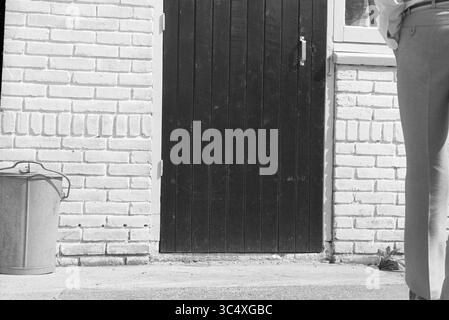 Le professeur Arnold Heertje retourne dans sa dernière cachette pendant la seconde Guerre mondiale : Schoolstraat 35 à Nieuw-Vennep. Il y a trouvé refuge à l'époque avec Janny et Cor Schreuders. La guerre demeure. Haarlemmermeer. Persons., Nieuw-Vennep, Schoolstraat, 16-06-1980 Whizgle News, Dutch Desk, pays-Bas, 1950-2000 Une personne se tient debout à côté d'une porte en bois, portant un pantalon de couleur claire, avec un seau en métal posé sur le sol à proximité. Les environs présentent un mur texturé fait de briques. Banque D'Images