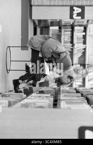 Enfants lisant dans la bibliothèque de Haarlem, Haarlem, pays-Bas, 05-11-1991 Whizgle News, Dutch Desk, pays-Bas, 1950-2000 Un enfant est assis pendu, profondément concentré sur un livre, niché sur un tabouret dans une bibliothèque entourée de rangées d'étagères remplies de livres. L'atmosphère reflète un sentiment de concentration tranquille et de curiosité. Banque D'Images