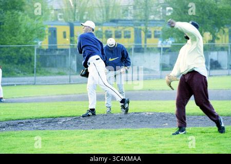 La première formation de l'équipe néerlandaise de baseball, 13-05-1997 Whizgle News, Dutch Desk, pays-Bas, 1950-2000 Un lanceur se retrouve sur le monticule alors qu'un batteur se prépare à se balancer, entouré de coéquipiers sur un terrain herbeux. La scène capture l'énergie et la concentration d'une pratique de baseball avec un train visible en arrière-plan. Banque D'Images