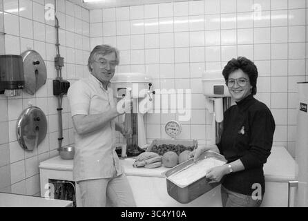 Glacier Tremonti Grote Houtstraat, crème glacée, patinoire, hockey sur glace, Haarlem, Grote Houtstraat, pays-Bas, 23-06-1988 Whizgle News, Dutch Desk, pays-Bas, 1950-2000 Un homme et une femme se tiennent debout dans une cuisine, souriant tout en préparant de la nourriture. L'homme tient un mélangeur, et la femme a un plateau rempli de dessert. Les fruits et légumes frais sont soigneusement disposés sur le comptoir, créant une scène culinaire animée. Banque D'Images
