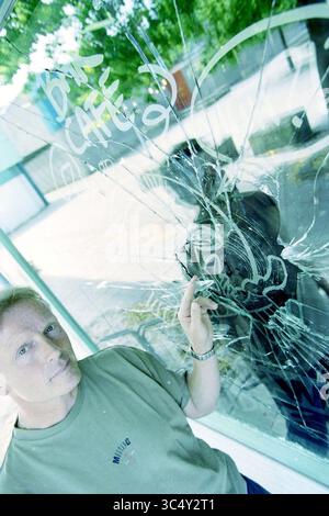 Café 'No Clue' fenêtre cassée, Nieuw-Vennep, Nieuw-Vennep, 16-07-2002 Whizgle News, Dutch Desk, pays-Bas, 1950-2000 Une personne se tient à côté d'une fenêtre brisée, pointant les dommages tandis qu'une réflexion est visible dans le verre. La fenêtre présente des graffitis, ajoutant au contexte urbain de la scène. Banque D'Images