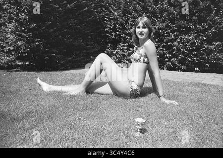 Miss de Angleterre, personnes, 23-07-1973 Whizgle News, Dutch Desk, pays-Bas, 1950-2000 Une jeune femme pose de manière ludique sur une pelouse, portant un bikini élégant. Elle est assise détendue, penchée légèrement en arrière avec une jambe tendue, tandis que la végétation luxuriante forme une toile de fond. Un objet décoratif repose à proximité sur l'herbe, ajoutant au charme décontracté de la scène. Banque D'Images