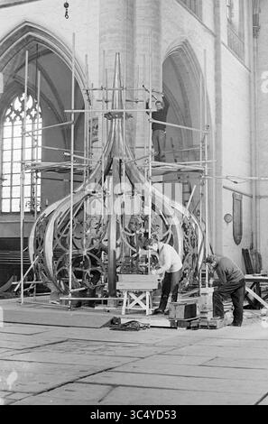 Travail sur l'oignon de la Grote ou de Sint-Bavokerk, tapotant les spinnacles au plomb, Grote Kerk Haarlem, églises Bavokerk, travail, Haarlem, Grote Markt, pays-Bas, 02-02-1965 Whizgle News, Dutch Desk, pays-Bas, 1950-2000 ouvriers sont vus construire un grand lustre orné dans un spacieux bâtiment voûté, entouré d'échafaudages. La conception complexe se caractérise par des formes curvilignes et fluides, et plusieurs individus sont engagés dans diverses tâches, tandis que la lumière pénètre à travers un grand vitrail en arrière-plan. Banque D'Images