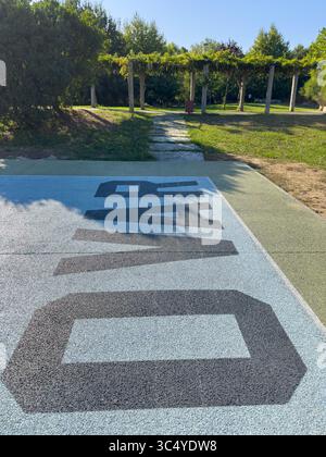 Grandes lettres noires orthographiant Ovar sur une surface texturée bleu clair et vert, avec un chemin de pierre menant à une tonnelle ombragée dans un parc ensoleillé. Banque D'Images
