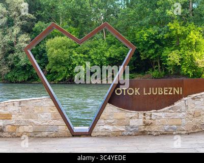 Beltinci, Slovénie - 18 juillet 2025 : cadre en forme de cœur près d'une rivière, entouré d'une végétation luxuriante. Le cadre est en métal et fait partie d'une pierre wa Banque D'Images