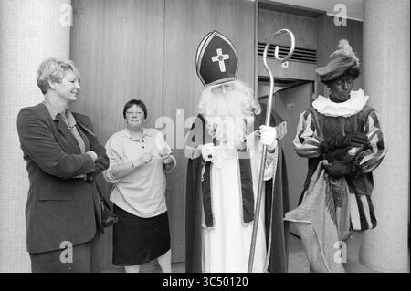 Nicholas en lien avec la natation scolaire, IJmuiden, pays-Bas, 01-12-1992 Whizgle News, Dutch Desk, pays-Bas, 1950-2000 Un groupe de trois individus se tient dans une pièce, l'un vêtu comme une figure sainte avec un bâton et des robes complexes, tandis que les autres observent - l'un semble être engagé dans la conversation, et l'autre est vêtu d'une tenue d'époque, ajoutant une touche festive et historique à la scène. Banque D'Images