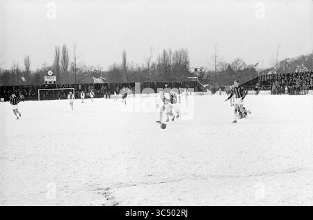 RCH - Ajax, Football, 17-02-1963 Whizgle News, Dutch Desk, pays-Bas, 1950-2000 Un match de soccer se déroule sur un terrain enneigé, avec des joueurs en uniformes contrastés qui se battent pour le ballon tandis qu’une foule regarde depuis les lignes de touche, entourés d’un paysage hivernal. Banque D'Images