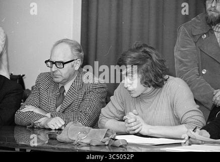Actions chez LES DSI formation sportive chez Duinlust Whizgle News, Dutch Desk, pays-Bas, 1950-2000 deux personnes s'assoient à une table, profondément réfléchies lors d'une réunion. L’un, portant des lunettes et un costume à carreaux, semble contemplatif, tandis que l’autre, vêtu d’un pull, a les mains serrées devant eux, concentrées sur la discussion. Un groupe de personnes peut être vu en arrière-plan, suggérant une atmosphère sérieuse. Banque D'Images