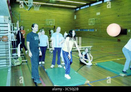 Cours de gymnastique anglais Linnaeus College, 10-12-2002 Whizgle News, Dutch Desk, pays-Bas, 1950-2000 Un groupe d'individus se livre à une activité de gymnase, une personne se préparant à lancer une grosse balle tandis que d'autres regardent ou participent à l'exercice. Le cadre comprend des paniers de basket-ball, des tapis de gymnastique et un intérieur en bois, créant une atmosphère animée de mouvement et de travail d'équipe. Banque D'Images
