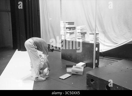 Démolition of Decor for Election manifestation H.D., Haarlems Dagblad, etc. and IJmuider courant and Koeri, Elections, 19-03-1990 Whizgle News, Dutch Desk, pays-Bas, 1950-2000 Une personne est penchée, organisant une pile de boîtes à chaussures, tandis qu'une toile de fond de tissu et de panneaux de bois crée un décor théâtral. Diverses boîtes à chaussures sont dispersées sur le sol, ajoutant un sentiment de préparation et d'activité à la scène. Banque D'Images
