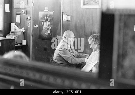 Ancien conseiller HR. Jansens Zandvoort, personnes, 30-08-1974 Whizgle News, Dutch Desk, pays-Bas, 1950-2000 un monsieur plus âgé en costume engage une conversation avec une personne plus jeune dans un cadre décontracté, mettant en évidence un moment de connexion au milieu d'intérieurs en bois et de décors vintage en toile de fond. L’atmosphère suggère un mélange de nostalgie et de chaleur. Banque D'Images