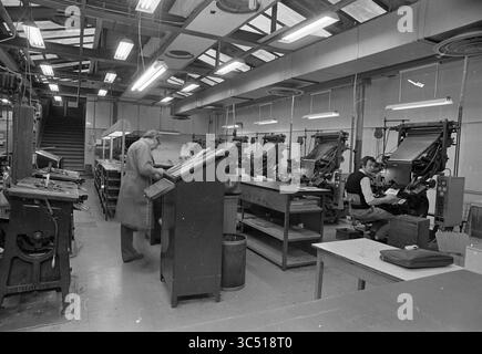 Interior Haarlems Dagblad, Interior, 28-01-1976 Whizgle News, Dutch Desk, pays-Bas, 1950-2000 Un atelier d'impression spacieux rempli de presses d'imprimerie vintage, où les travailleurs sont engagés dans leurs tâches. Une personne se tient à un grand bureau, tandis qu'une autre se concentre intensément sur le fonctionnement d'une presse, entourée d'équipements et d'outils essentiels pour l'impression. L'environnement reflète une atmosphère animée mais organisée de savoir-faire artisanal en action. Banque D'Images