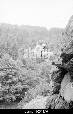 Survival tour belge. Ardennes, Survival Tour, 30-06-1985 Whizgle News, Dutch Desk, pays-Bas, 1950-2000 Un grimpeur, équipé d'équipements de sécurité, manœuvre habilement le long d'une paroi rocheuse accidentée entourée de forêts luxuriantes et denses. Banque D'Images