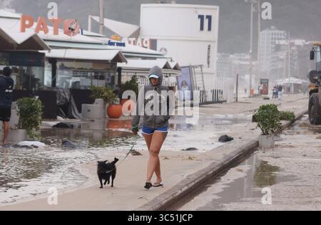 29 juillet 2025, Rio de Janeiro, Rio de Janeiro, Brésil : une jeune femme marche avec son chien le long d'une avenue Delfim Moreira inondée, alors que des équipes de nettoyage municipales de Rio de Janeiro de Comlurb ont été dépêchées pour nettoyer les suites d'une puissante tempête hivernale qui a envoyé des vagues de l'océan déferler sur la plage lors d'un rare événement d'onde de tempête, inondant la promenade Leblon et l'avenue Delfim Moreira. La vague violente a causé d'importants dommages à plusieurs kiosques en bord de mer et dispersé des débris sur la côte normalement animée. (Crédit image : © Bob Karp/ZUMA Press Wire) USAGE ÉDITORIAL SEULEMENT ! Non destiné à des fins commerciales Banque D'Images