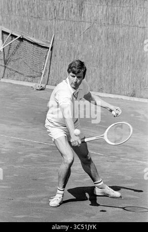 Tennis match Whizgle News, Dutch Desk, pays-Bas, 1950-2000 Un joueur de tennis est sur le point de faire du swing, axé sur la frappe de la balle avec précision sur le court. Vêtu d'une tenue classique, il affiche des prouesses athlétiques sur fond d'un filet et d'une surface texturée. Banque D'Images