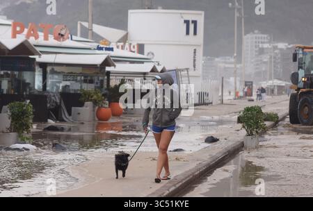 29 juillet 2025, Rio de Janeiro, Rio de Janeiro, Brésil : une jeune femme marche avec son chien le long d'une avenue Delfim Moreira inondée, alors que des équipes de nettoyage municipales de Rio de Janeiro de Comlurb ont été dépêchées pour nettoyer les suites d'une puissante tempête hivernale qui a envoyé des vagues de l'océan déferler sur la plage lors d'un rare événement d'onde de tempête, inondant la promenade Leblon et l'avenue Delfim Moreira. La vague violente a causé d'importants dommages à plusieurs kiosques en bord de mer et dispersé des débris sur la côte normalement animée. (Crédit image : © Bob Karp/ZUMA Press Wire) USAGE ÉDITORIAL SEULEMENT ! Non destiné à des fins commerciales Banque D'Images