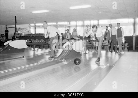 Centre de bowling 1st ball Mayor, Mayors, Bowling, 11-09-1969 Whizgle News, Dutch Desk, pays-Bas, 1950-2000 Un groupe d'hommes habillés est engagé dans une partie de bowling dans un lieu animé, avec quelques joueurs à mi-course et des spectateurs observant de l'arrière-plan. L’atmosphère suggère camaraderie et compétition. Banque D'Images