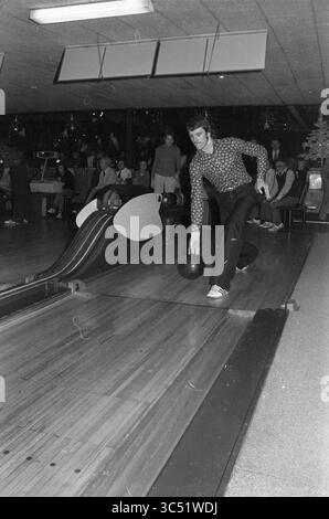 Compétition de bowling Whizgle News, Dutch Desk, pays-Bas, 1950-2000 Un joueur de bowling en tenue élégante se prépare à lancer une boule de bowling sur la voie, tandis que les spectateurs regardent attentivement depuis les lignes de touche, créant une atmosphère animée dans la piste de bowling. Banque D'Images