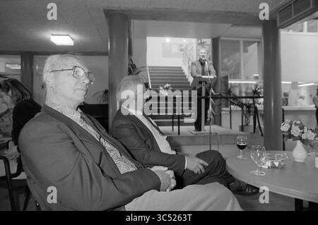 Adieu Jan de Bruin à l'OBNL, Haarlem, pays-Bas, 18-06-1991 Whizgle News, Dutch Desk, pays-Bas, 1950-2000 deux messieurs sont assis au premier plan, l'un portant des lunettes et une veste à motifs, tandis que l'autre est en costume. En arrière-plan, un conférencier se tient sur un podium dans un escalier, s’adressant à un public. Une petite table au premier plan tient un verre de vin et un vase de fleurs. L'atmosphère suggère un événement formel ou un rassemblement. Banque D'Images