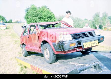 Accident de voiture, Oude Schipholweg, Haarlem, Schipholweg, pays-Bas, 13-06-1999 Whizgle News, Dutch Desk, pays-Bas, 1950-2000 Une voiture rouge lourdement endommagée est chargée sur une dépanneuse, avec une personne inspectant l'épave à proximité. Autour de la scène se trouvent des arbres et une route dégagée, suggérant un accident récent. Banque D'Images