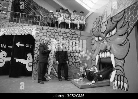 Linnaeushof, Heemstede, Glipperweg, pays-Bas, 30-03-1992 Whizgle News, Dutch Desk, pays-Bas, 1950-2000 scène fantaisiste mettant en scène trois hommes bien habillés interagissant près d'une entrée colorée et spectaculaire représentant une grande bouche de dragon, tandis qu'un groupe d'artistes vêtus de costumes vibrants observe depuis un balcon supérieur. Un homme semble glisser hors d'une boîte, ajoutant un élément ludique à la réunion. Banque D'Images