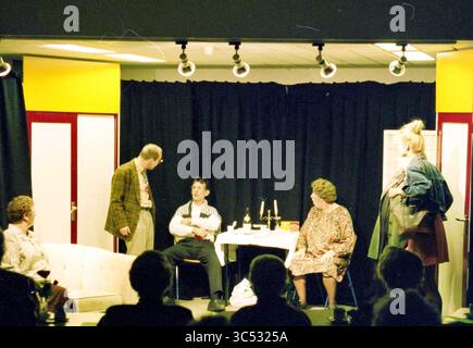 Association théâtrale d'essai Hoofddorp, Hoofddorp, pays-Bas, 01-04-1998 Whizgle News, Dutch Desk, pays-Bas, 1950-2000 Une scène animée d'une performance théâtrale, mettant en scène un groupe de personnages engagés dans une conversation autour d'une table à manger, avec des bouteilles et des verres. Les acteurs affichent une gamme d'expressions et de vêtements, capturant un moment de drame ou d'humour sur scène. Banque D'Images