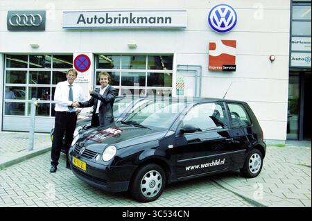 Auto Brinkmann présente Marco Borsato avec une Volkswagen avec War Child promotion, Haarlem, pays-Bas, 09-08-2001 Whizgle News, Dutch Desk, pays-Bas, 1950-2000 deux hommes se tiennent devant un concessionnaire automobile, tenant fièrement les clés devant une petite voiture noire arborant un logo de charité. La concession présente des enseignes pour Audi et Volkswagen en arrière-plan, soulignant une atmosphère de célébration et de nouveaux débuts. Banque D'Images