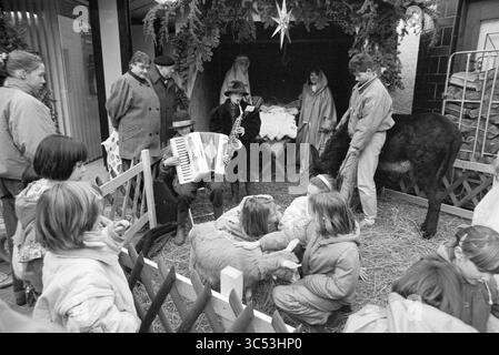 Scène vivante de la nativité J. van Gooyenstraat, Noël et arbres de Noël, Heemstede, Jan van Goyenstraat, pays-Bas, 24-12-1988 Whizgle News, Dutch Desk, pays-Bas, 1950-2000 scène festive représentant un groupe d'enfants rassemblés autour d'une scène de nativité, où des interprètes représentent des personnages clés tandis que d'autres jouent d'instruments de musique. Les animaux sont présents, améliorant l'atmosphère animée, tandis que les spectateurs apprécient l'affichage avec un sentiment d'émerveillement. Banque D'Images