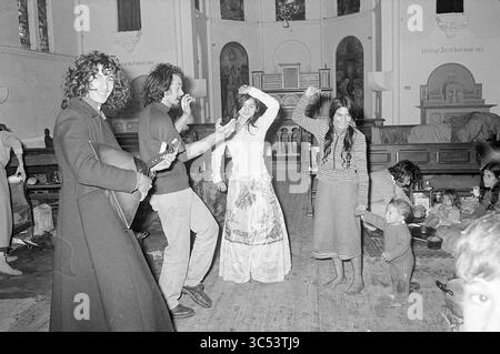 Gitans à Ruigoord, Gitans, 25-10-1973 Whizgle News, Dutch Desk, pays-Bas, 1950-2000 Un groupe d'individus joyeux s'engage dans une danse animée à l'intérieur d'une salle spacieuse, ornée de meubles en bois et de détails artistiques. Une personne joue d'un instrument à cordes, tandis que d'autres bougent rythmiquement, montrant un esprit de liberté et de célébration. Les enfants sont présents, observant les festivités avec curiosité. Banque D'Images
