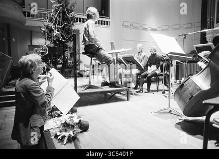 Rep. NPhO, ton de Leeuw, 20-12-1994 Whizgle News, Dutch Desk, pays-Bas, 1950-2000 Un chef d'orchestre dirige un petit ensemble, engagé dans une répétition musicale, tandis qu'un flûtiste est assis sur le sol, axé sur la musique en partitions. Les décorations évoquent une ambiance festive, avec un sapin de Noël subtilement situé en arrière-plan. Banque D'Images
