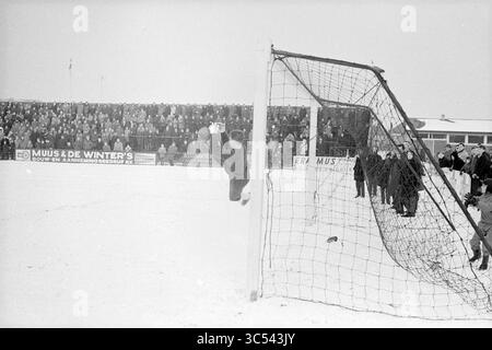 RCH - Ajax, Football, 17-02-1963 Whizgle News, Dutch Desk, pays-Bas, 1950-2000 Un gardien de but saute pour faire une sauvegarde spectaculaire lors d'un match de football enneigé, tandis qu'une foule nombreuse regarde depuis les gradins, créant une atmosphère d'excitation et de tension. Banque D'Images